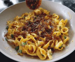 Delicious caramelized onion pasta drizzled with spicy chili oil on a rustic plate.