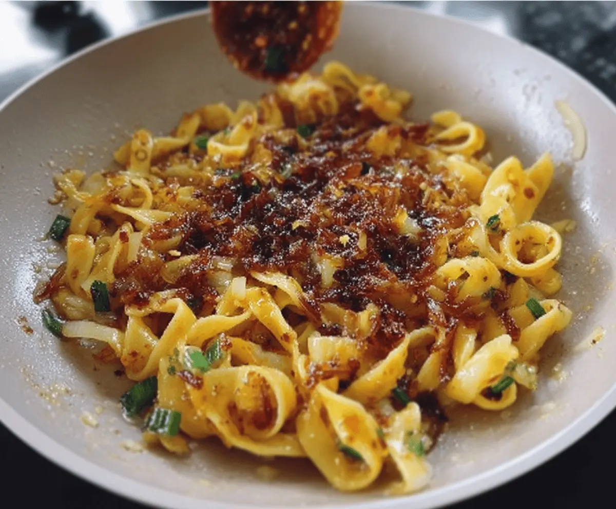 Delicious caramelized onion pasta drizzled with spicy chili oil on a rustic plate.