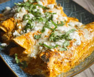 Creamy pumpkin chicken enchiladas topped with melted cheese and fresh cilantro on a plate, served with a side of salsa and sour cream