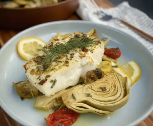 Delicious roasted halibut served with artichokes and lemon slices on a elegant plate.
